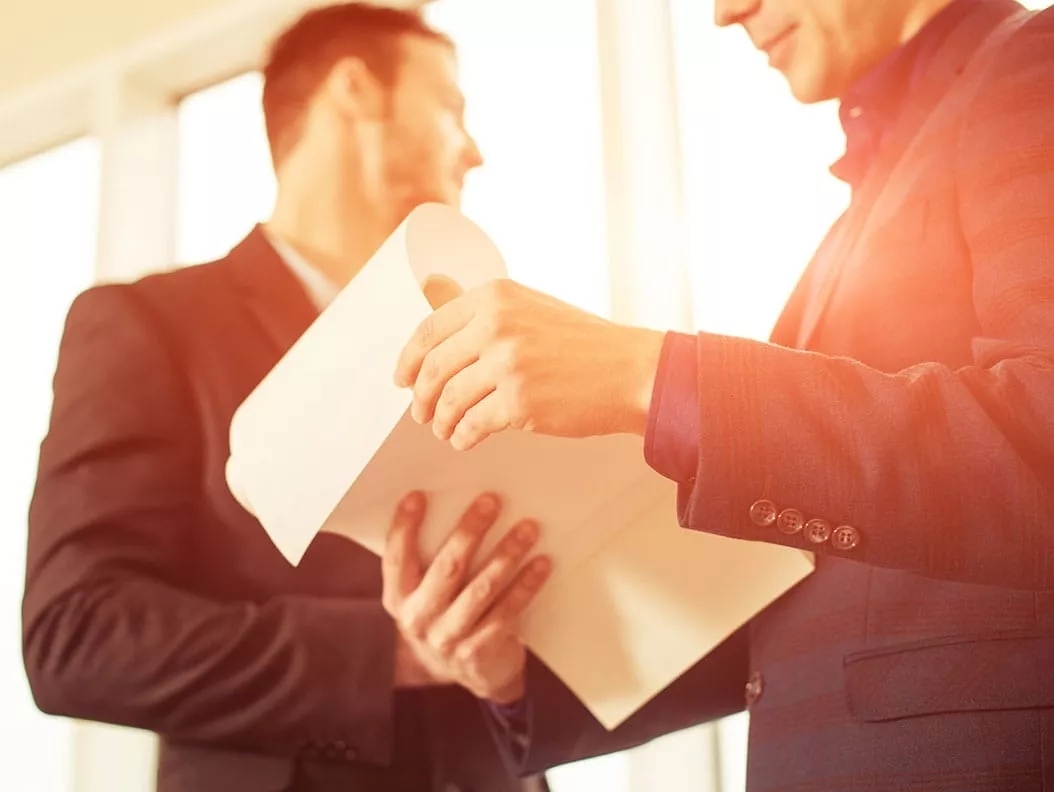 Two men wearing a suit viewing and flipping a packet of papers.