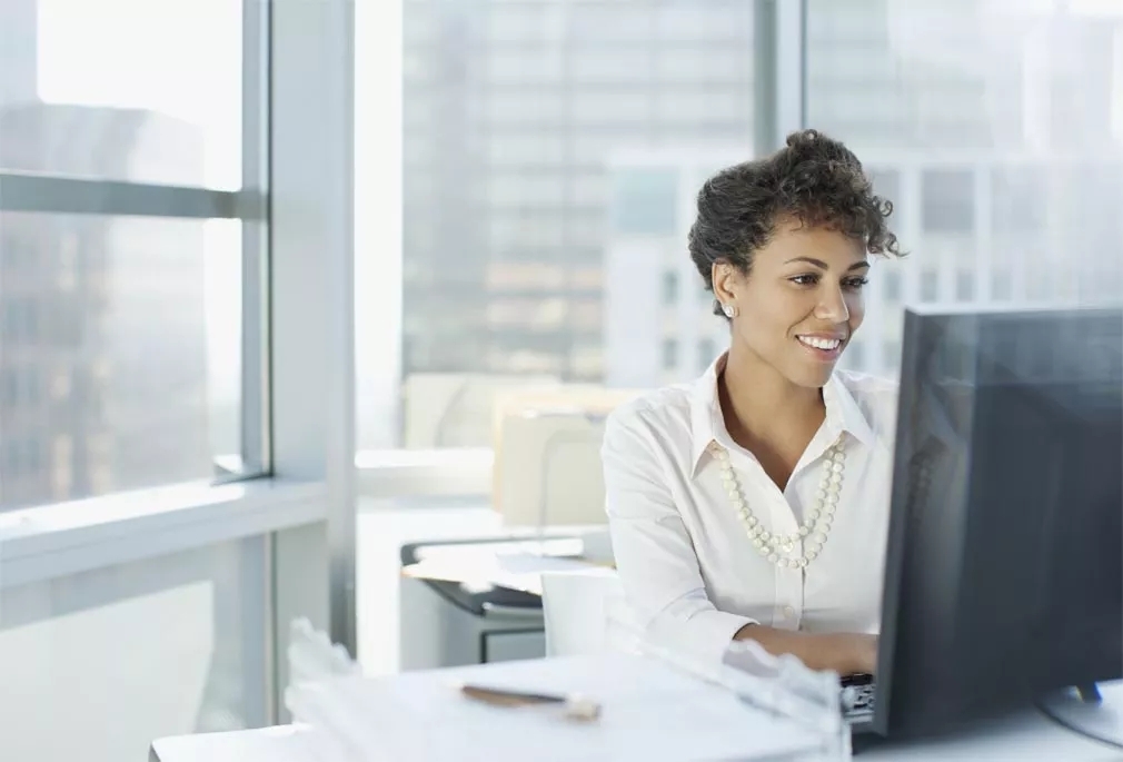 A women wearing a white shirt and working on the computer at her desk.