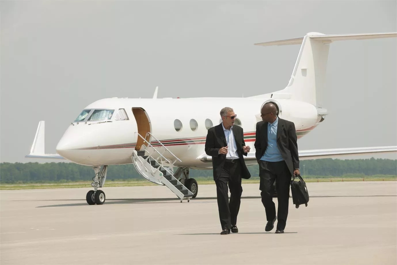 Two people walking on the runway, away from a plane in the background.