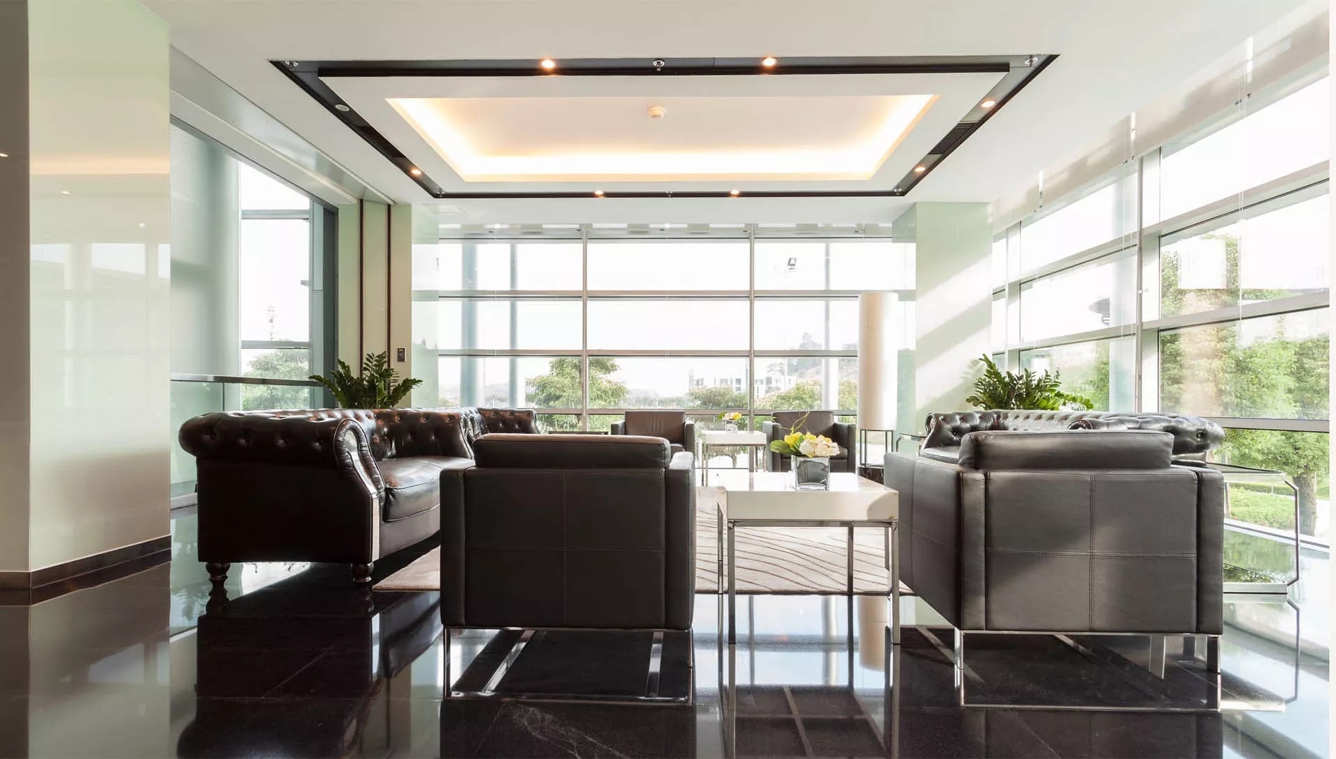 A well lit, glass surrounded, corporate welcome room with many chairs and couches.