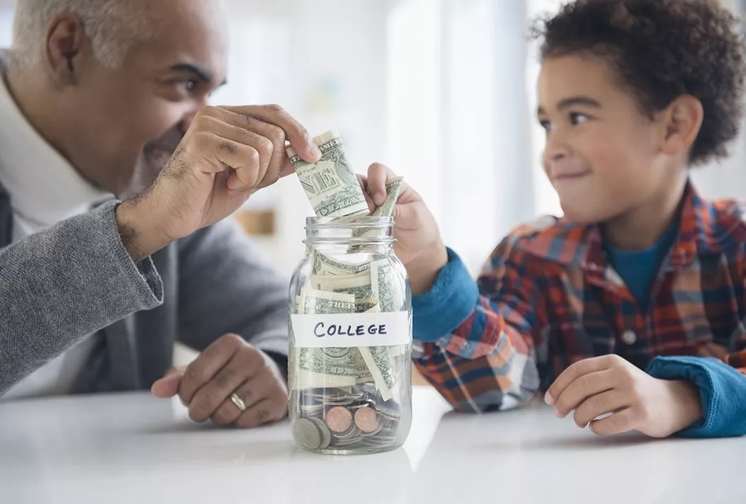 A father and son each putting money into a jar labeled 'College'.
