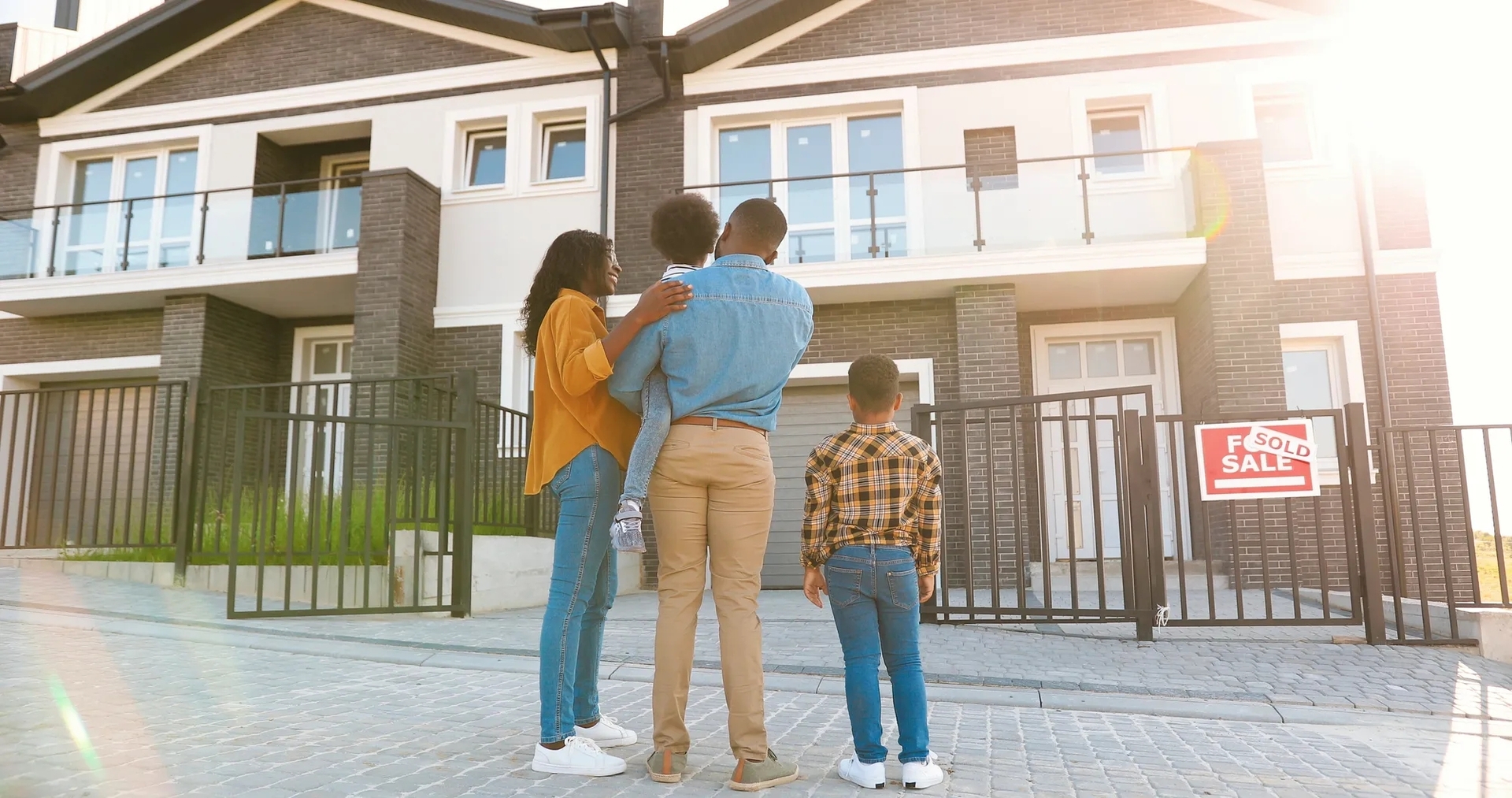 Family standing in front of a house with a sold sign with their backs facing the camera