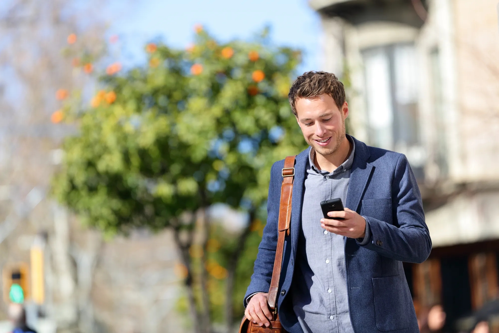 A man holding a phone in the foreground and a tree and building out of focus in the background A man holding a phone in the foreground and a tree and building out of focus in the background
