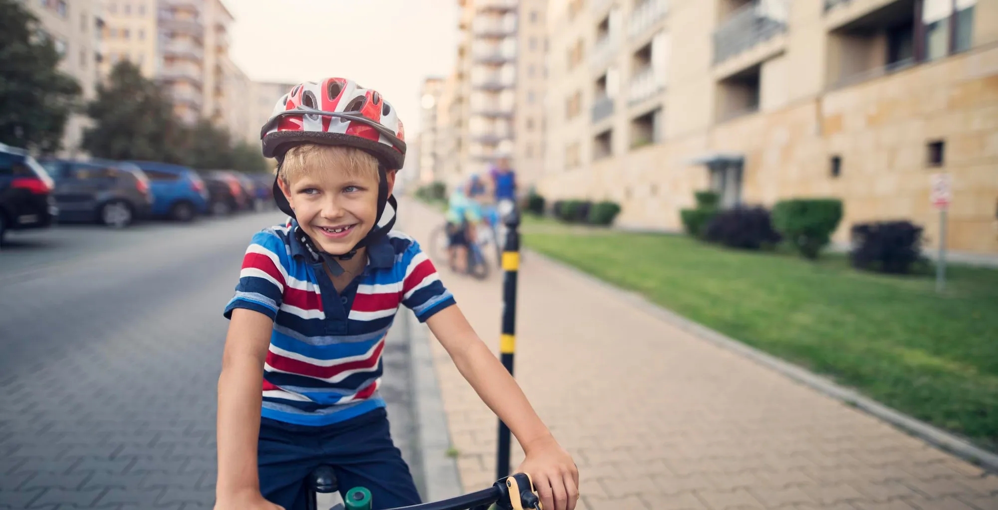 Little boy in a blue, white, and red striped shirt wearing a red and white helmet on a bicycle.