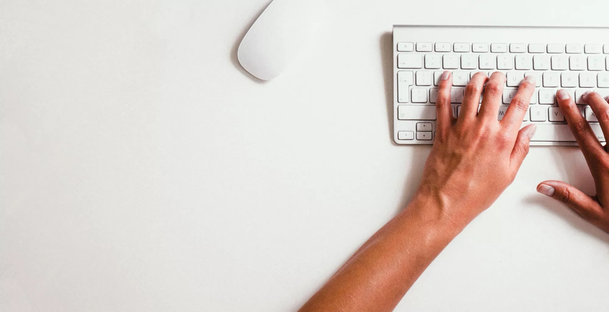 A person typing on a keyboard with a mouse to the side.