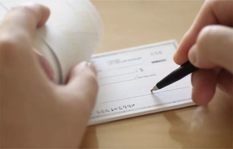 A close up of a pair of hands signing a check.