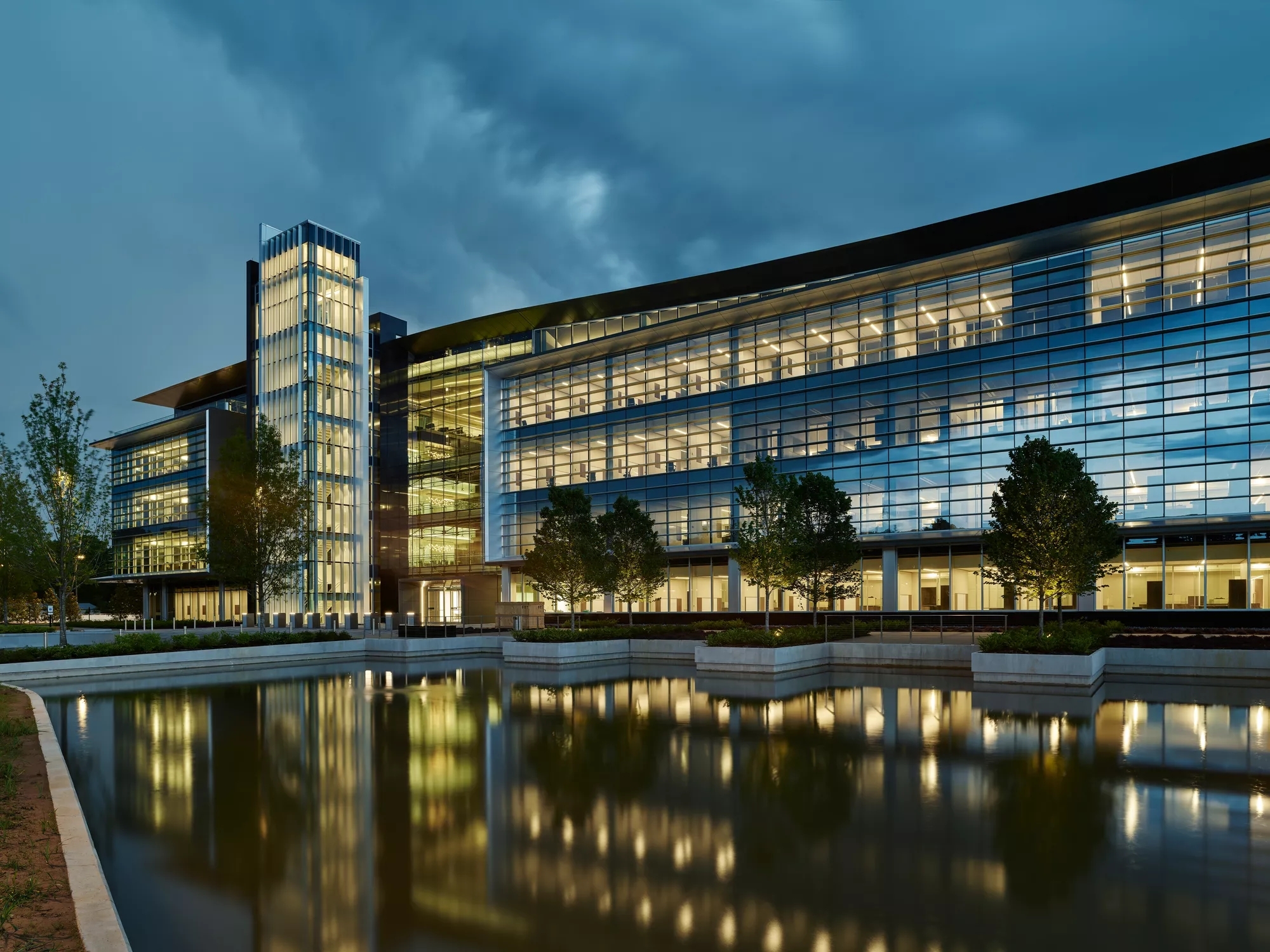 Bank OZK Headquarters at night with many lights lit up, reflecting off the pond in front.