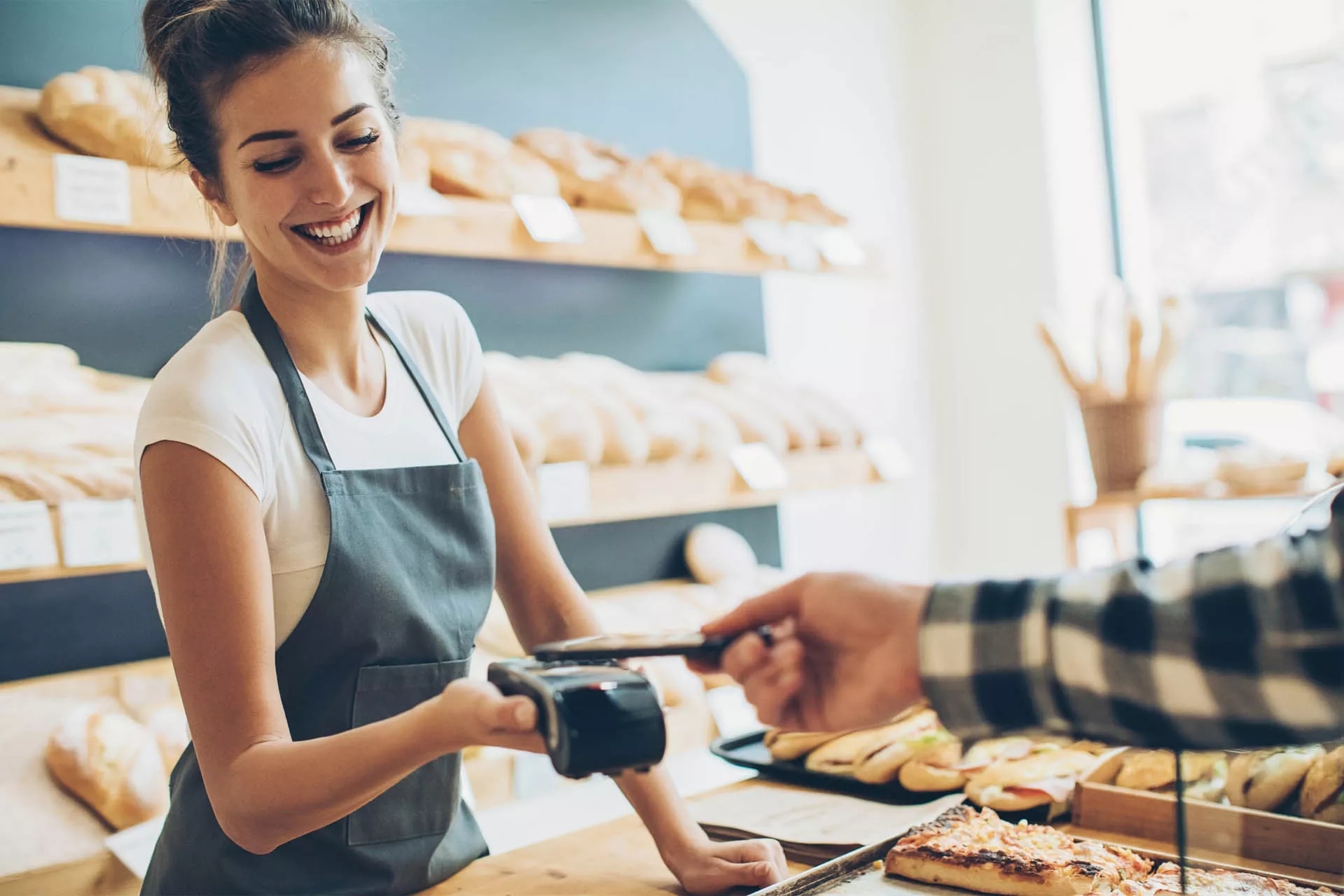 A woman behind the counter at a bakery completing a touchless payment transaction.