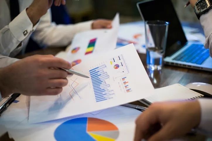 A close up of the table featuring graphs on paper being discussed by two sets of arms.