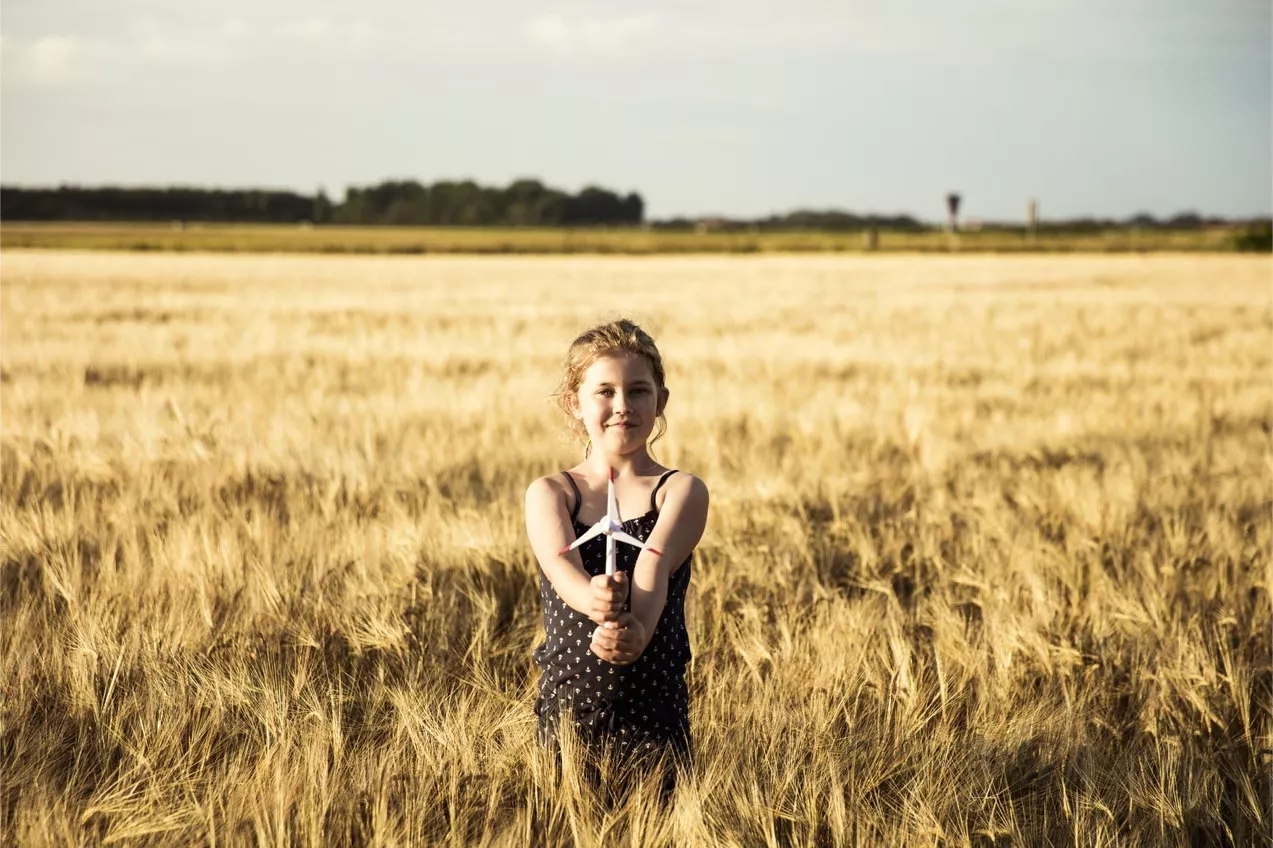 A smiling girl holding a pinwheel standing in a wheat field.
