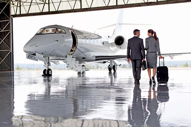 Two people walking across a hangar towards a parked aircraft.