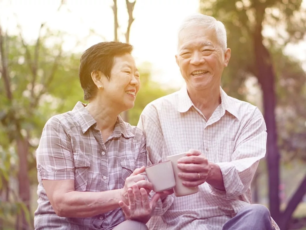 A man and a woman sitting and holding mugs in their hands and smiling.