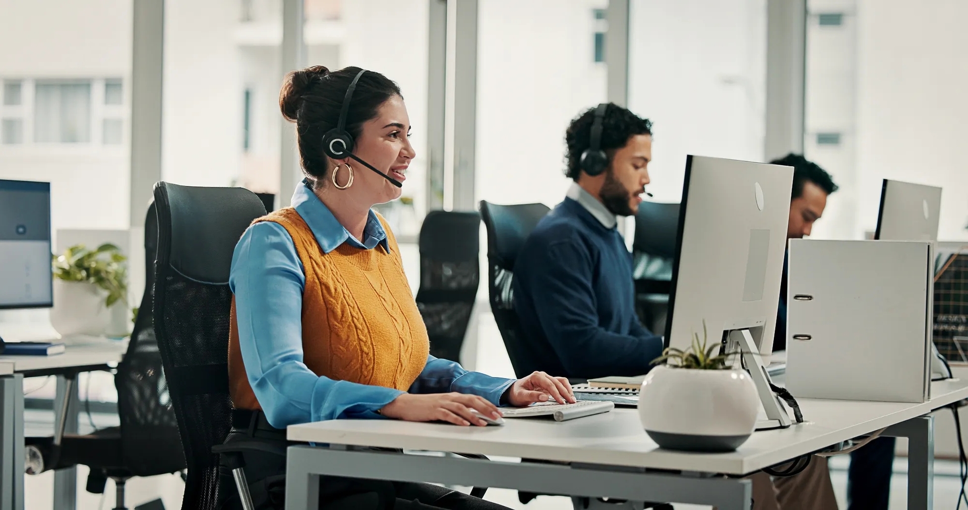 Three call center employees sitting at computers wearing headsets Three call center employees sitting at computers wearing headsets