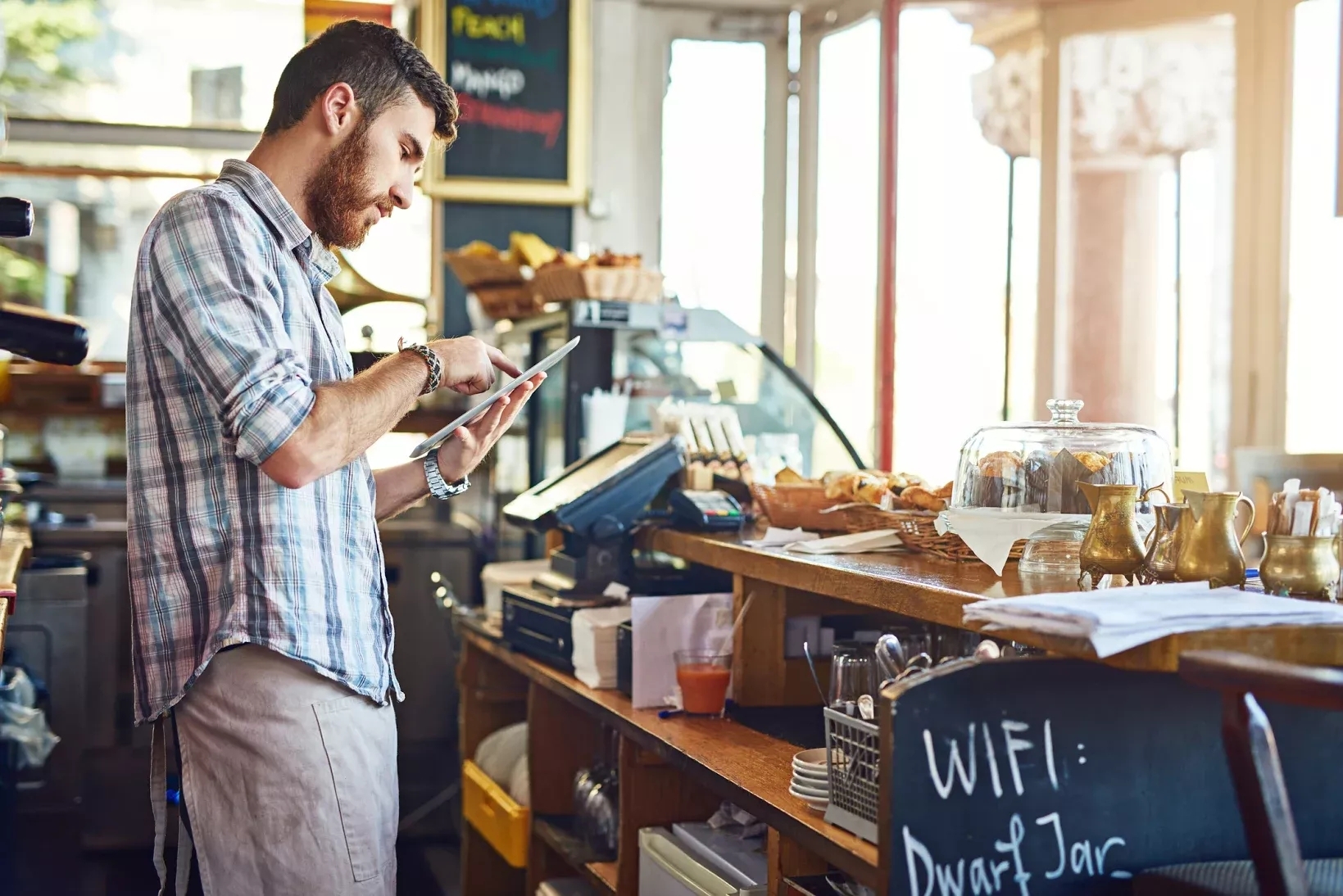 A coffee shop owner working on tablet behind counter A coffee shop owner working on tablet behind counter