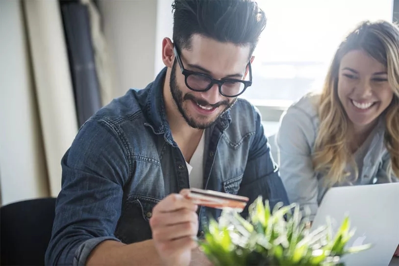 A person wearing glasses smiling down at a credit card held up below him in the foreground.