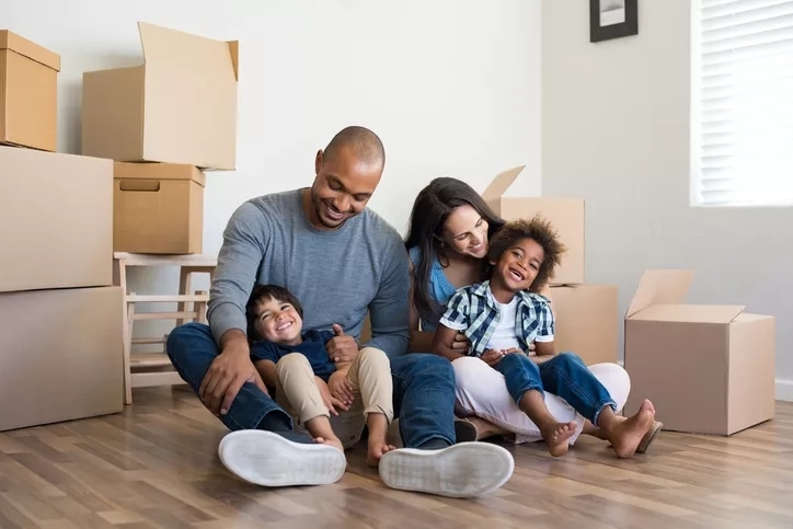 A family unpacking in their new home. Their two children sit in their laps among open cardboard boxes.
