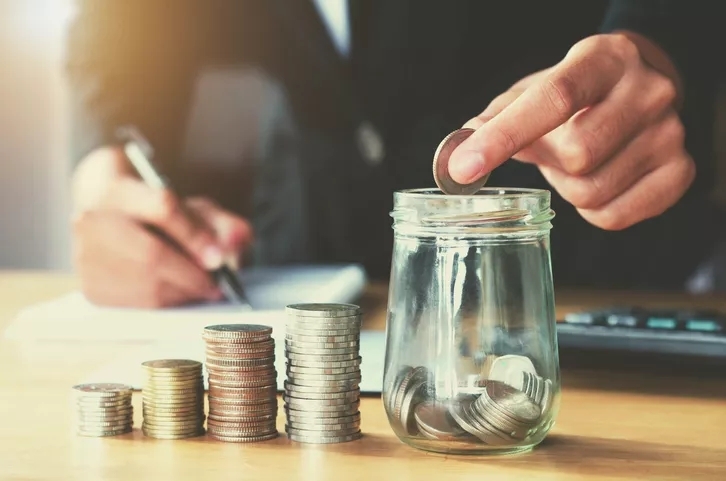 A person counting stacked coins into a jar.