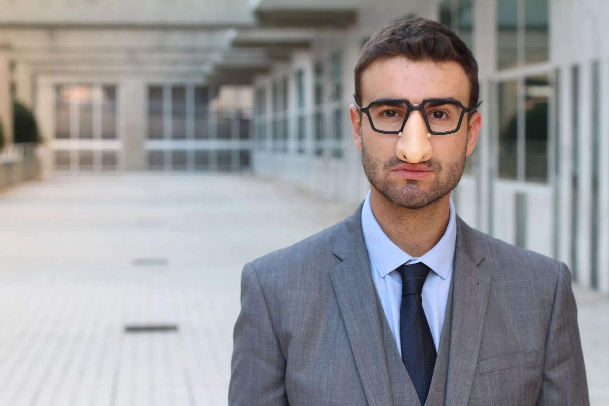 A person wearing suit and black glasses and an eyeglasses with fake nose.