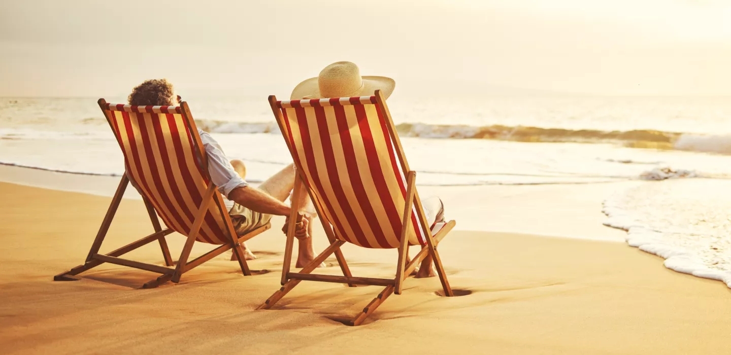 A couple holding hands facing away on the beach near the surf, in wood and fabric beach chairs. A couple holding hands facing away on the beach near the surf, in wood and fabric beach chairs.