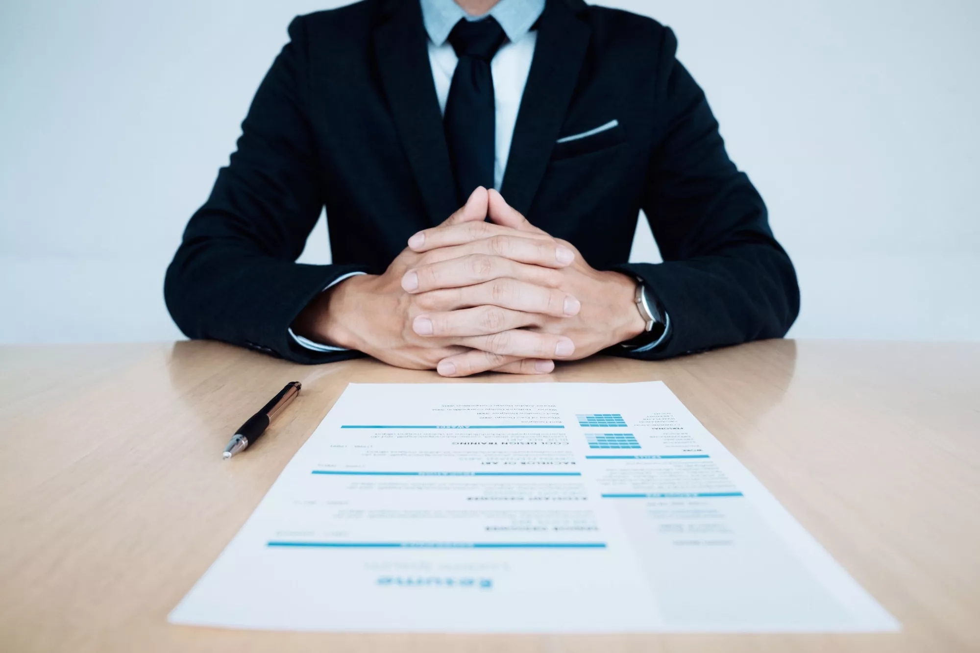 A person wearing a suit sits across the table, an application form and pen in front of them.