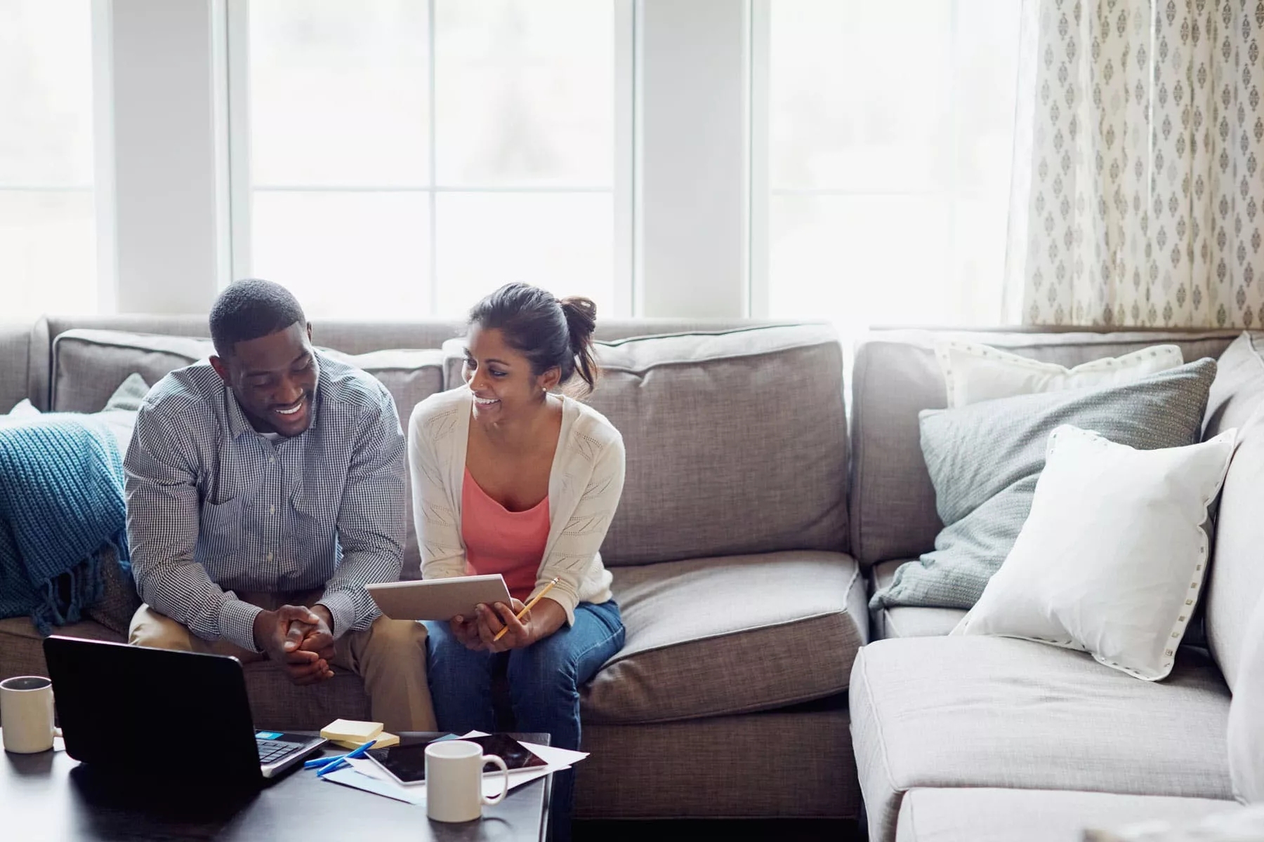 Man and a women sitting on a couch and discussing and has laptop before them on the coffee table.