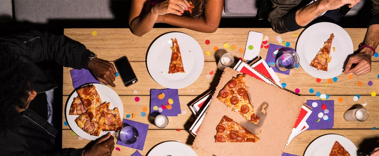 A top down view of a group of people at a picnic table eating pizza. Controversially, there are slices both with and without pineapple on them.