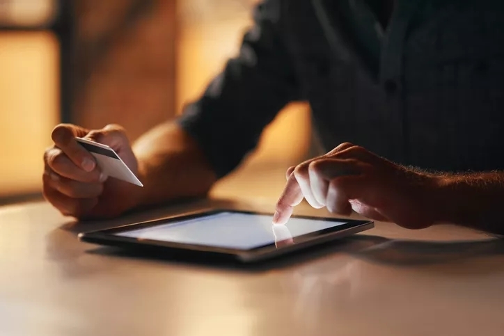 A person looking at their credit card and tablet on a table.