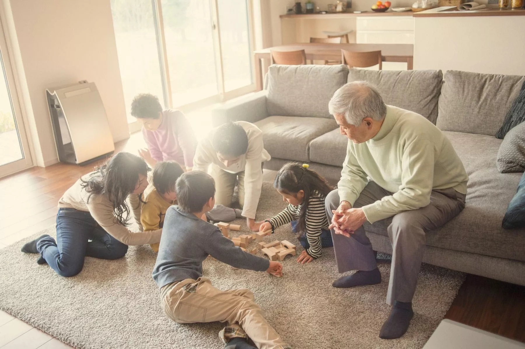 A family with three children, three adults, and two elderly people playing a board game half on the couch, half on the floor.