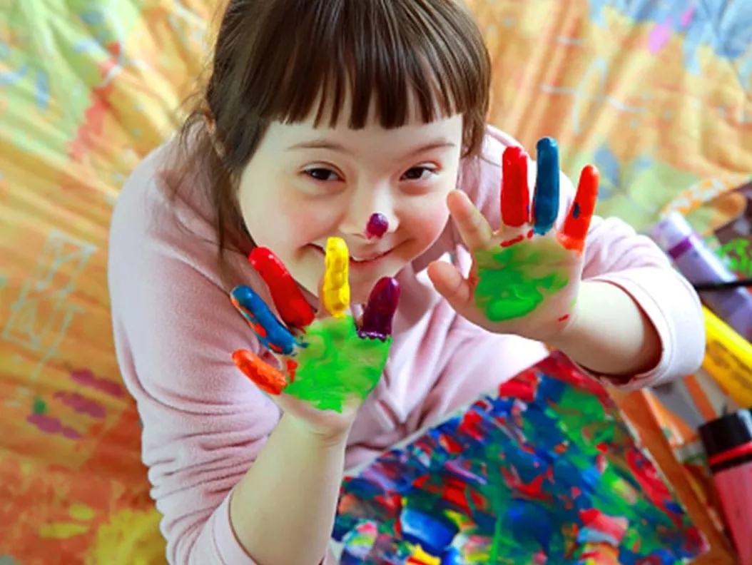 A young girl with finger paint on her hands and the art below her.